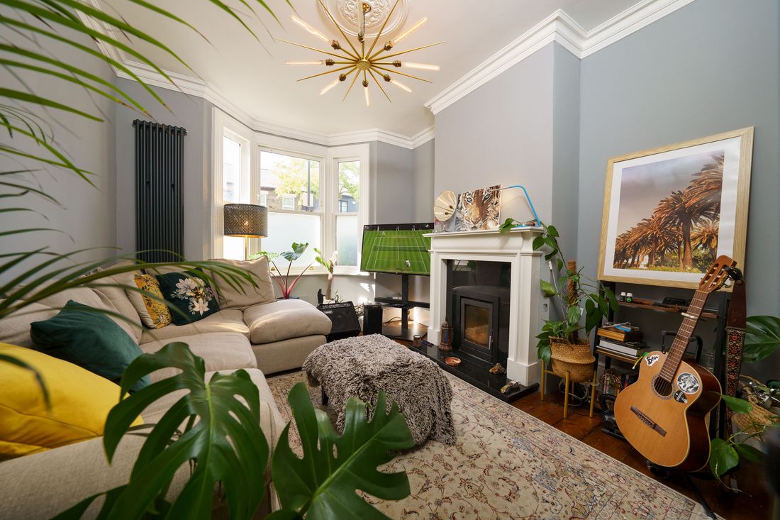 Victorian living room with bay window, fireplace, plants and warm furnishings in East London