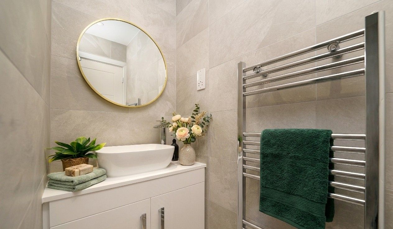 Spotless bathroom with round brass mirror, white basin, plants and fresh towels on a heated rail