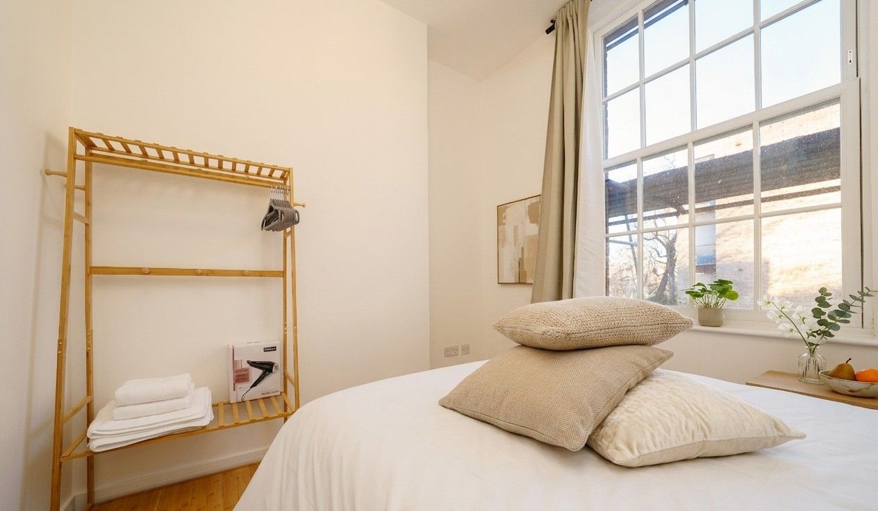 Plump pillows on a freshly made white bed beside a bamboo rail with folded towels