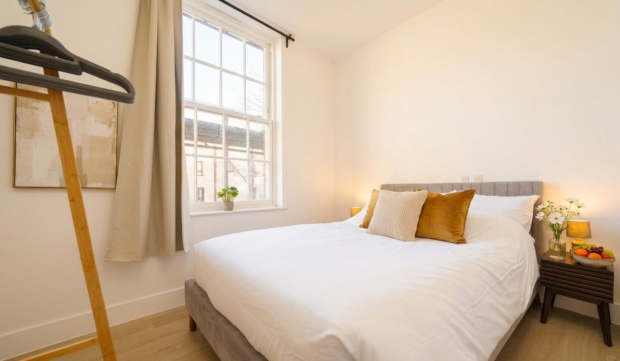 Freshly made double bed with crisp white linen and gold cushions beside a sash window