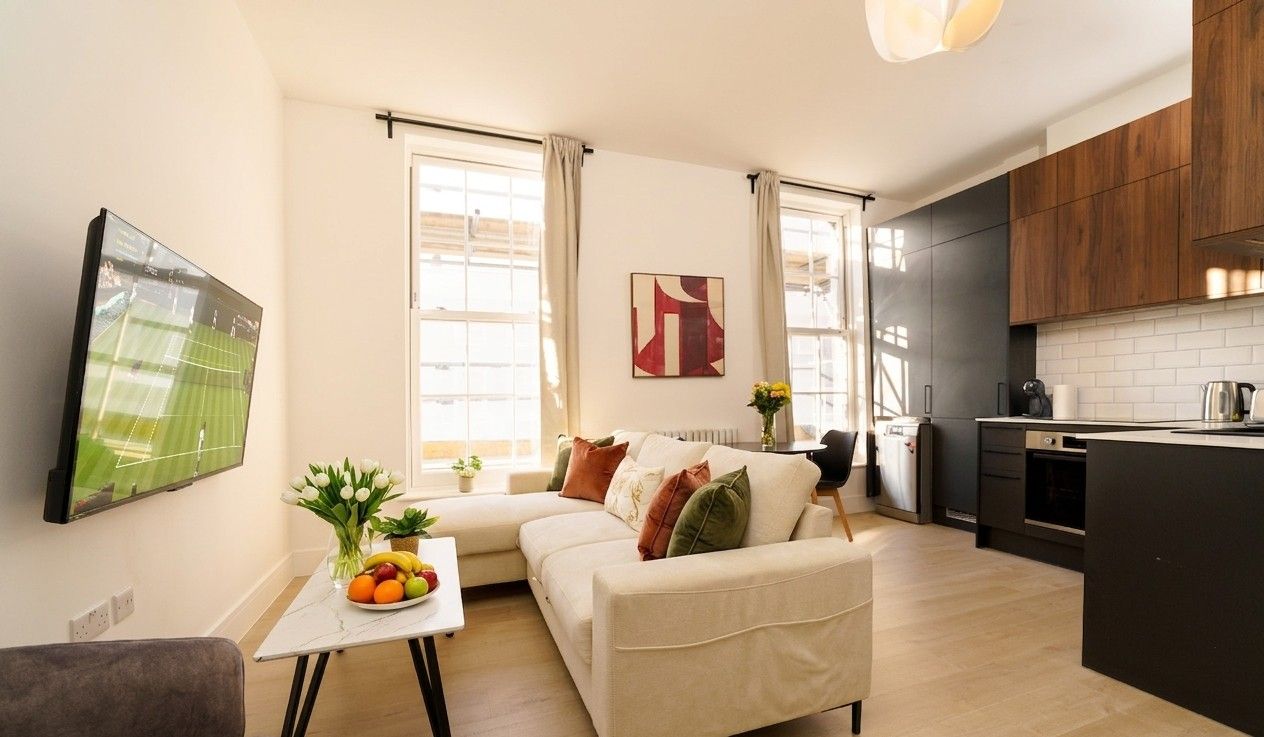 Bright living room with tall sash windows, cream sofa, fresh tulips and an open kitchen in a Camden apartment